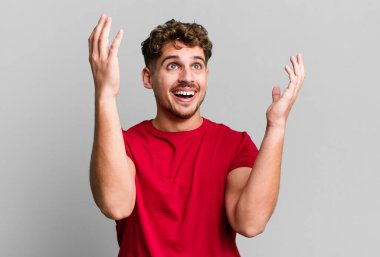 young adult caucasian man feeling happy, amazed, lucky and surprised, celebrating victory with both hands up in the air