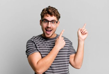 young adult caucasian man feeling joyful and surprised, smiling with a shocked expression and pointing to the side