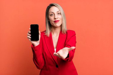 pretty blonde woman smiling happily with friendly and  offering and showing a concept. businesswoman showing a phone screen