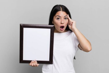İspanyol güzel kadın şaşırmış görünüyor, boş bir çerçeve ile yeni bir düşünce, fikir veya konsept gerçekleştiriyor.