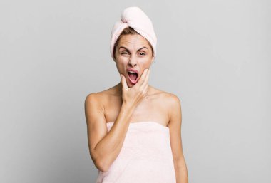 hispanic pretty woman with mouth and eyes wide open and hand on chin wearing pbathrobe. beauty concept