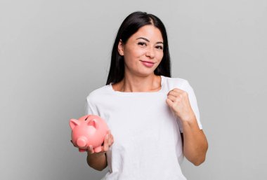 hispanic pretty woman looking arrogant, successful, positive and proud with a piggy bank