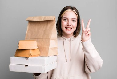young pretty woman smiling and looking happy, gesturing victory or peace. take away fast food concept
