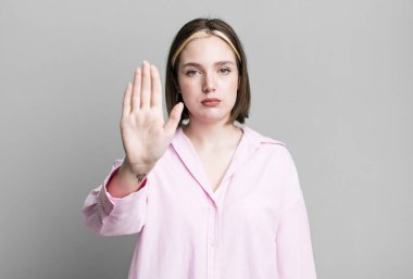 Genç ve güzel bir kadın ciddi görünüyor. Avuç içini gösteriyor. Dur hareketi yapıyor.