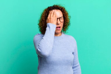 Orta yaşlı İspanyol bir kadın uykulu, sıkılmış ve esniyor, baş ağrısı ve yüzünün yarısını kaplayan bir elle.