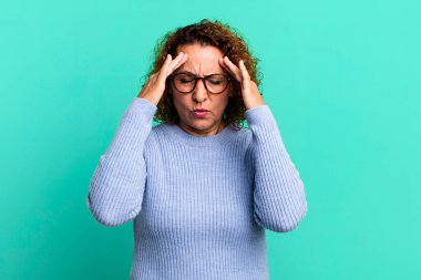 Orta yaşlı İspanyol kadın stresli ve hayal kırıklığına uğramış görünüyor, baskı altında çalışıyor ve başı ağrıyor.