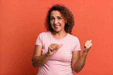 Orta yaşlı İspanyol kadın neşeli bir şekilde gülümsüyor ve yan taraftaki fotokopi alanını işaret ediyor, mutlu ve tatmin olmuş hissediyor.