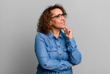 Orta yaşlı İspanyol kadın mutlu bir şekilde gülümsüyor ve hayal kuruyor ya da şüphe ediyor.