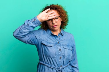 Orta yaşlı İspanyol kadın stresli, yorgun ve hayal kırıklığına uğramış görünüyor, alnından ter damlıyor, umutsuz ve bitkin hissediyor.