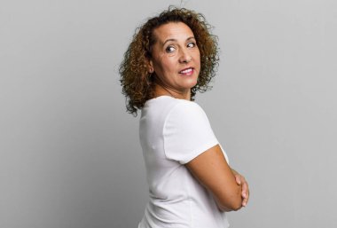 Orta yaşlı İspanyol kadın neşeyle gülümsüyor, mutlu, tatmin olmuş ve rahatlamış hissediyor, kollarını kavuşturup yan tarafa bakıyor.