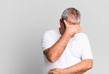 Orta yaşlı bir adam stresli, utanmış ya da üzgün görünüyor, baş ağrısı var, yüzünü eliyle kapatıyor.