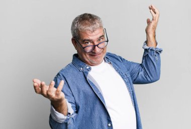 middle age senior man shrugging with a dumb, crazy, confused, puzzled expression, feeling annoyed and clueless