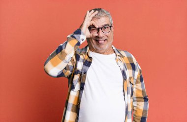 Orta yaşlı bir adam mutlu bir şekilde gülümsüyor, şaka yapıyor ve gözetleme deliğinden bakıyor, sırları gözetliyor.