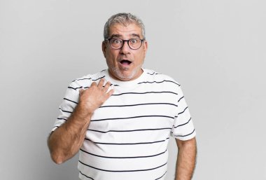 Orta yaşlı bir adam şok olmuş, şaşırmış ve şaşırmış hissediyor, elleri göğsünde ve ağzı açık, kim olduğunu söylüyor, ben mi??