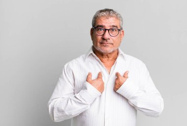 Orta yaşlı bir adam, kafası karışık ve tuhaf bakışlarıyla kendini işaret ediyor. Seçildiği için şaşırmış ve şaşırmış görünüyor.