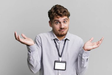 young adult caucasian man feeling puzzled and confused and doubting. blank accreditation pass card id concept