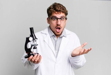 young adult caucasian man feeling extremely shocked and surprised. scients laboratory student with a microscope concept