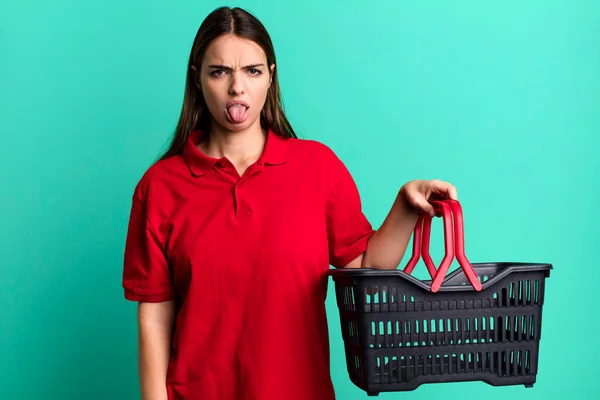 young pretty woman feeling disgusted and irritated and tongue out. empty shopping basket concept