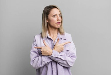 blonde adult woman looking puzzled and confused, insecure and pointing in opposite directions with doubts