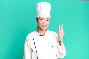 pretty asian woman smiling and looking friendly, showing number three. restaurant chef concept