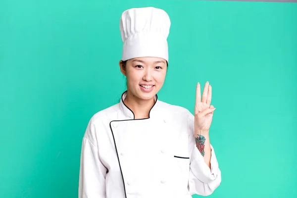 pretty asian woman smiling and looking friendly, showing number three. restaurant chef concept