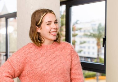 pretty caucasian woman with cheerful, carefree, rebellious attitude, joking and sticking tongue out, having fun. home interior concept