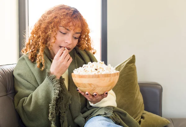 年轻的红头发姑娘漂亮的女人在沙发上吃爆米花 看电影 — 图库照片