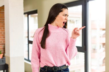pretty caucasian woman feeling joyful and surprised, smiling with a shocked expression and pointing to the side