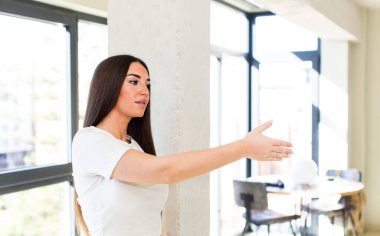 young adult pretty woman smiling, greeting you and offering a hand shake to close a successful deal, cooperation concept