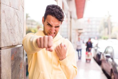 Genç İspanyol adam kendinden emin, sinirli, güçlü ve agresif görünüyor. Yumrukları boks pozisyonunda dövüşmeye hazır.