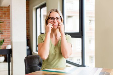 Genç ve güzel bir kadın gülümsüyor ve sahte gülüşüne işaret ediyor.