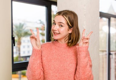 pretty caucasian woman smiling and looking happy, friendly and satisfied, gesturing victory or peace with both hands. home interior concept