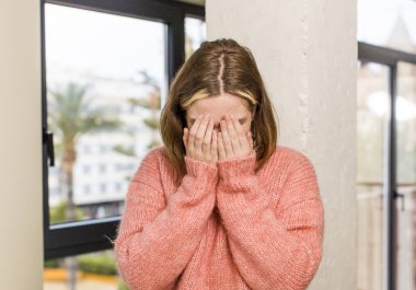 Kafkasyalı bir kadın üzgün, hayal kırıklığına uğramış, gergin ve depresif, iki eliyle yüzünü kaplayan, ağlayan. ev içi konsept