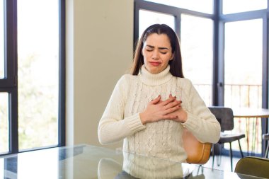 pretty caucasian woman looking sad, hurt and heartbroken, holding both hands close to heart, crying and feeling depressed