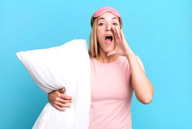 Güzel sarışın kadın kendini mutlu hissediyor, elleri ağzının kenarında bağırıyor. Pijama ya da gecelik konsepti