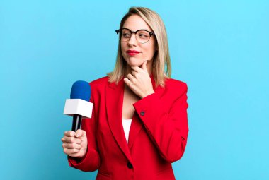 pretty blonde woman smiling with a happy, confident expression with hand on chin. presenter or journalist with a microphone