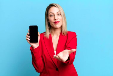 pretty blonde woman smiling happily with friendly and  offering and showing a concept. businesswoman showing a phone screen