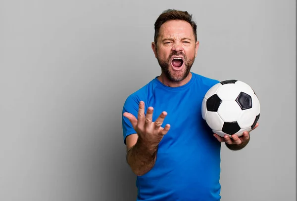 middle age man looking angry, annoyed and frustrated. with a soccer ball. fitness concept
