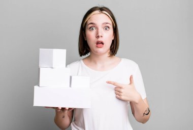 Şok olmuş ve ağzı açık, kendini gösteren genç ve güzel bir kadın. beyaz boş kutular