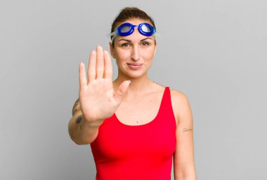 Genç ve güzel bir kadın ciddi görünüyor. Avuç içini gösteriyor. Durdurma hareketi yapıyor. yüzücü kavramı