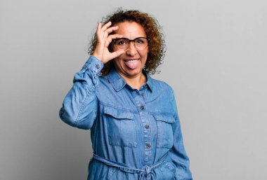 Orta yaşlı İspanyol kadın mutlu bir şekilde gülümsüyor, şaka yapıyor ve gözetleme deliğinden bakıyor, sırları gözetliyor.