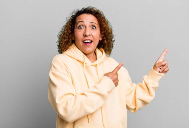 Orta yaşlı İspanyol kadın neşeli ve şaşırmış hissediyor, şok olmuş bir ifadeyle gülümsüyor ve yan tarafı işaret ediyor.