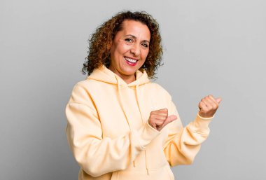 Orta yaşlı İspanyol kadın neşeli bir şekilde gülümsüyor ve yan taraftaki fotokopi alanını işaret ediyor, mutlu ve tatmin olmuş hissediyor.