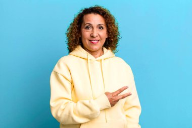 Orta yaşlı İspanyol kadın mutlu, pozitif ve başarılı hissediyor. Göğsünde el yapımı V ile zafer ya da barış gösteriyor.