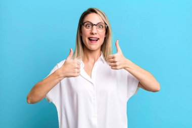 blonde adult woman smiling broadly looking happy, positive, confident and successful, with both thumbs up