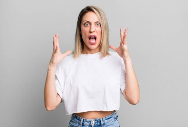 blonde adult woman screaming with hands up in the air, feeling furious, frustrated, stressed and upset