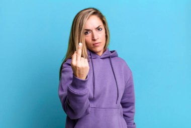 blonde adult woman feeling angry, annoyed, rebellious and aggressive, flipping the middle finger, fighting back