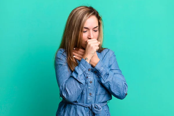blonde adult woman feeling ill with a sore throat and flu symptoms, coughing with mouth covered