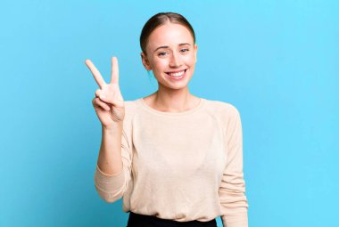 Gülümsüyor ve dost canlısı görünüyor. İki ya da iki numarayı gösteriyor. Elini ileri uzatıp geri sayıyor.