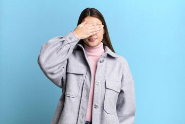 pretty young adult woman covering eyes with one hand feeling scared or anxious, wondering or blindly waiting for a surprise